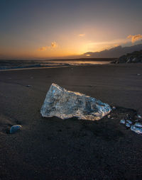 Iceberg on shore at beach against sky during sunset