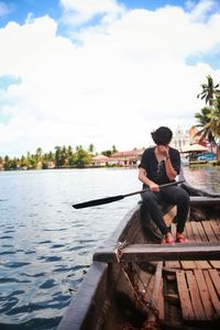 Man sitting on boat in lake against sky