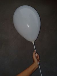 Close-up of hand holding balloons against white background