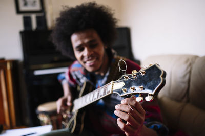 Young male guitarist adjusting strings of instrument at home