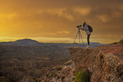Rear view of man standing on mountain against sky during sunset