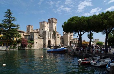 Boats in river by buildings in city against sky