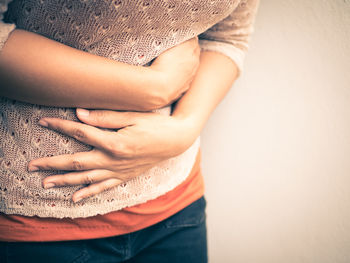 Midsection of woman with stomachache standing against beige background