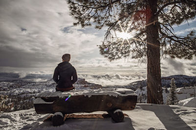 Woman sits on snow covered bench overlooking bryce canyon after snow