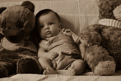 Baby boy sitting by teddy bears on sofa