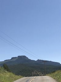 Road leading towards mountains against clear blue sky