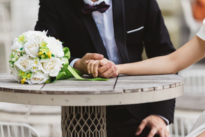 Couple holding hands by rose bouquet during wedding ceremony