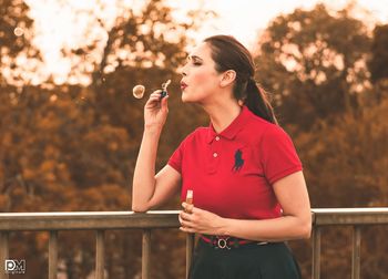Beautiful woman standing by railing against trees