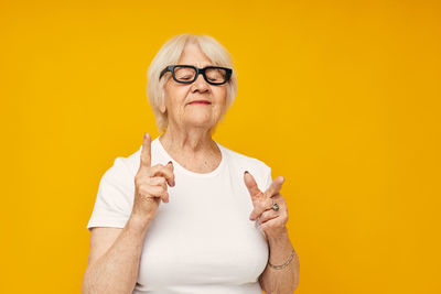 Senior woman gesturing against yellow background