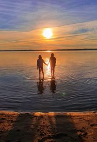 Silhouette people on beach against sky during sunset