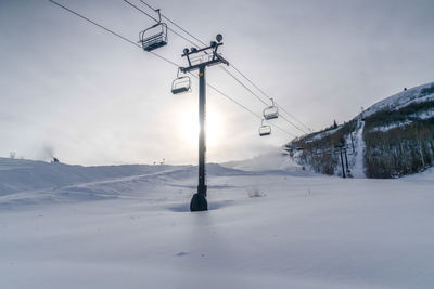 Electricity pylon on snow covered field against sky