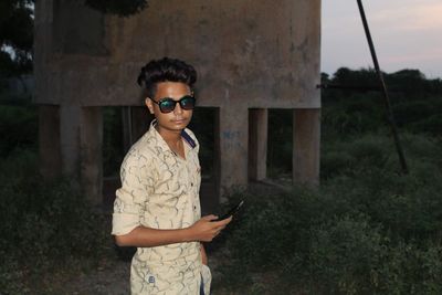 Young man holding mobile standing against water tank outdoors