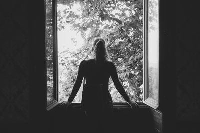 Rear view of woman looking through window at home