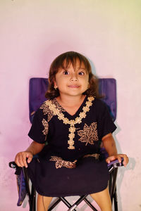 Portrait of young woman sitting on chair against wall