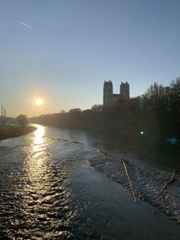 Scenic view of river by buildings against sky at sunset