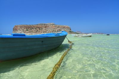 Boats moored on beach against clear blue sky