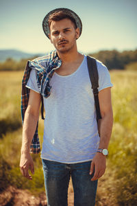 Portrait of young man standing on field against sky