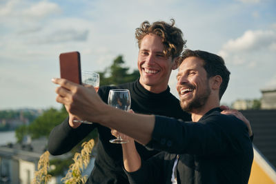 Cheerful male friends taking selfie with mobile phone on terrace