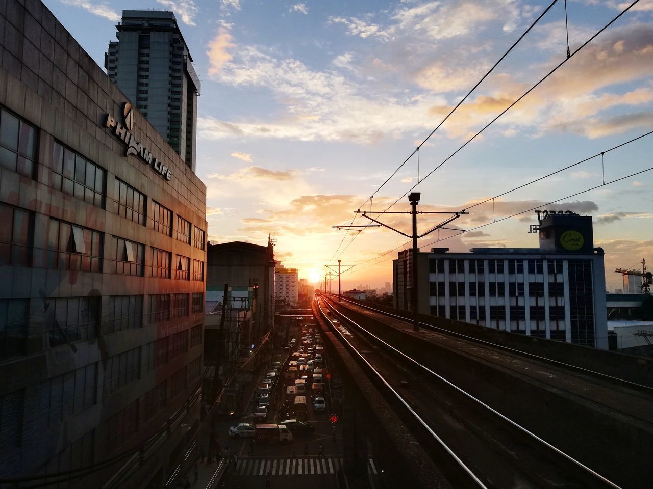 RAILROAD TRACKS AMIDST BUILDINGS AGAINST SKY DURING SUNSET