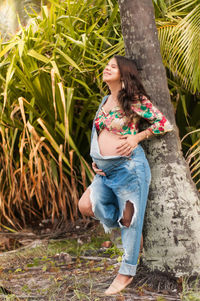 Full length of pregnant woman standing by tree trunk