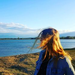 Teenage girl looking away on field by lake against sky