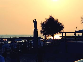 Silhouette statue by sea against orange sky