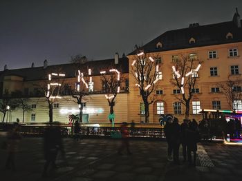 People walking on illuminated street against buildings at night