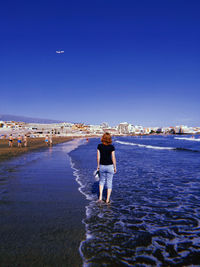 Rear view of woman standing at beach against clear blue sky