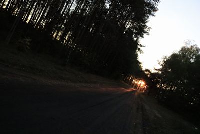 Road amidst trees in forest against sky at sunset