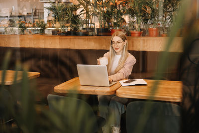 A business woman with glasses works online using a laptop. shot through a window