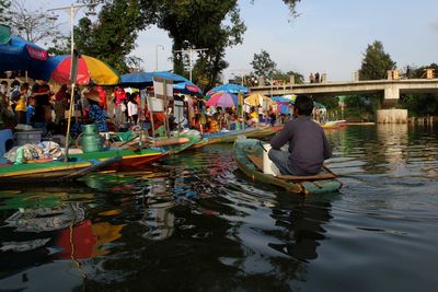 People sitting on riverbank against sky