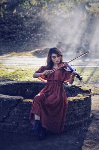 Woman playing violin while sitting on well