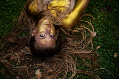 Close-up of young woman lying on grass , her body is completely covered with glitter