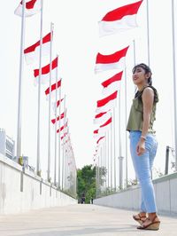 Side view of woman standing on bridge by flags against sky