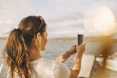 Woman taking selfie through mobile phone against lake during summer vacation