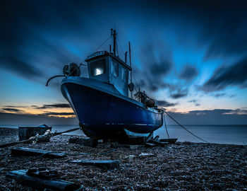 Abandoned boat moored on shore against sky during sunset