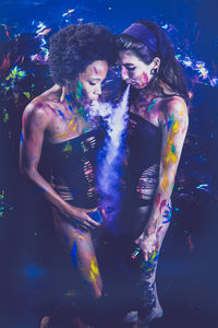 Friends covered in power paint while smoking electronic cigarette in holi at night