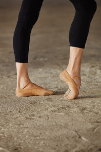 Crop faceless ballet dancer in black leotard and pointe shoes stretching legs with pose on concrete floor