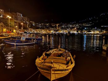 Boats moored on sea against illuminated city at night