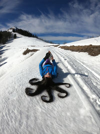 Woman using mobile phone while lying on snow field against sky