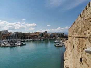 Sailboats moored on sea by buildings against sky