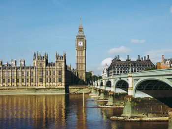 Arch bridge over river by buildings against sky in city