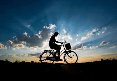 Silhouette man riding bicycle against cloudy sky during sunset