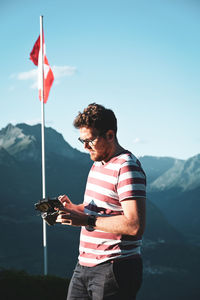Young man using drone remote control against sky and mountains 