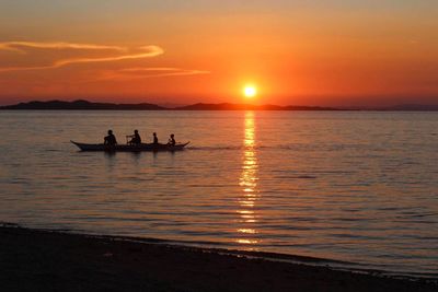 Silhouette people on sea against sky during sunset