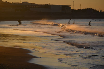 Silhouette people on beach by sea against sky during sunset