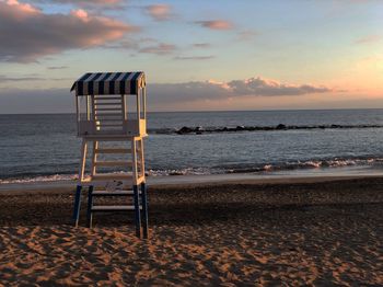 Lifeguard chair on beach against sky during sunset