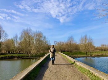 Woman walking by lake against sky