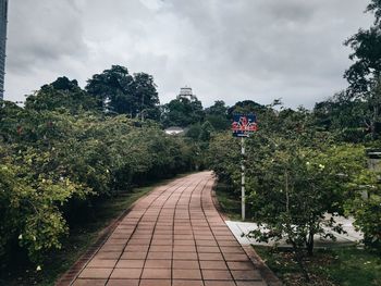 Walkway amidst trees against sky