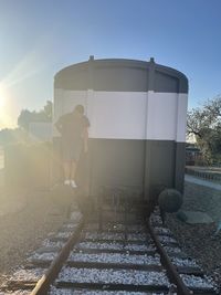 Rear view of man standing on railroad track against sky